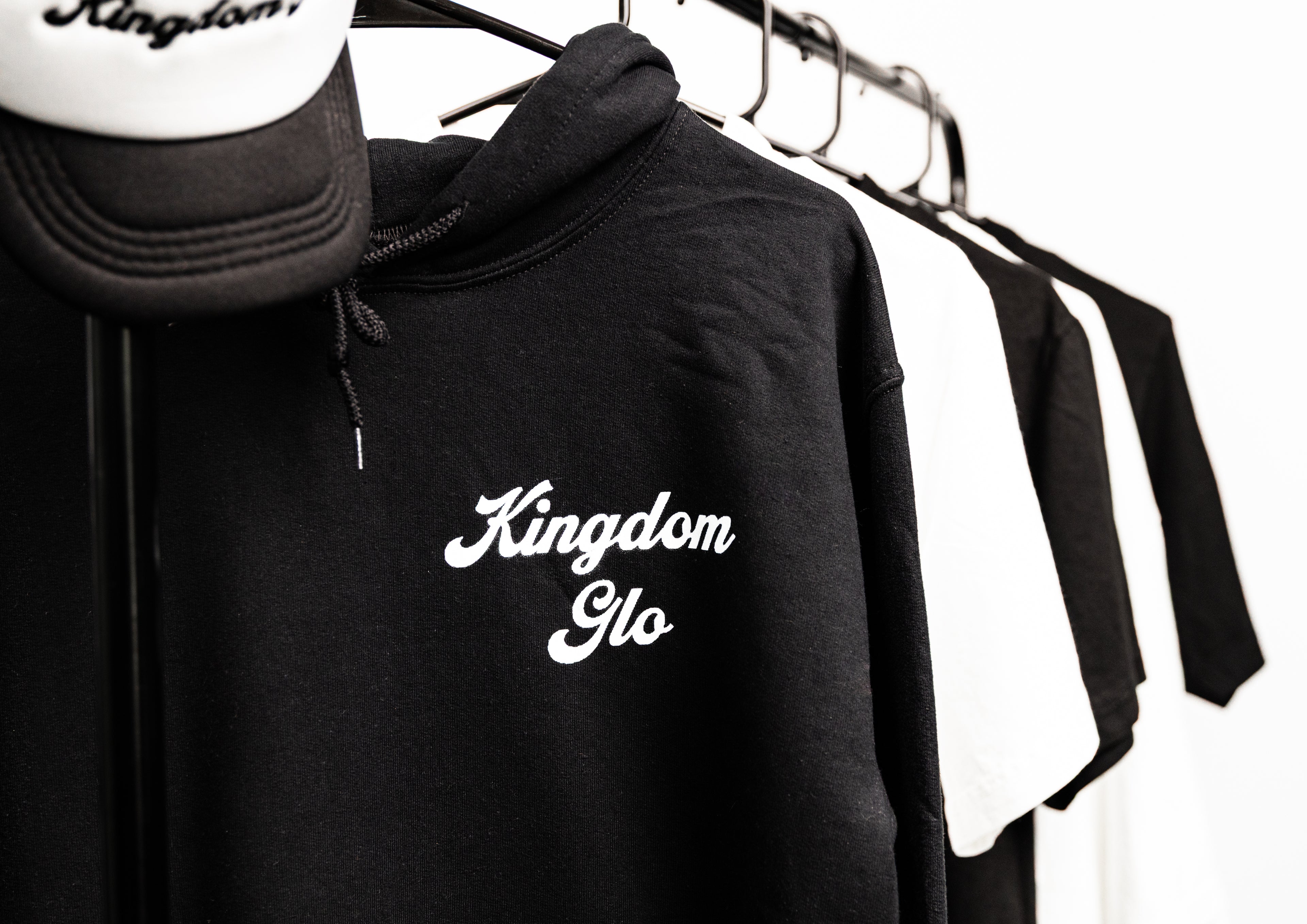 Black hoodie with 'Kingdom Glo' branding on a rack with other clothing items.